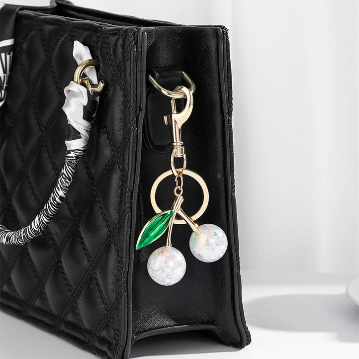 Modern Grace Pearlie Cherry Drop with Leaf keychain bag charm hanging from a purse, featuring a cherry and leaf design.