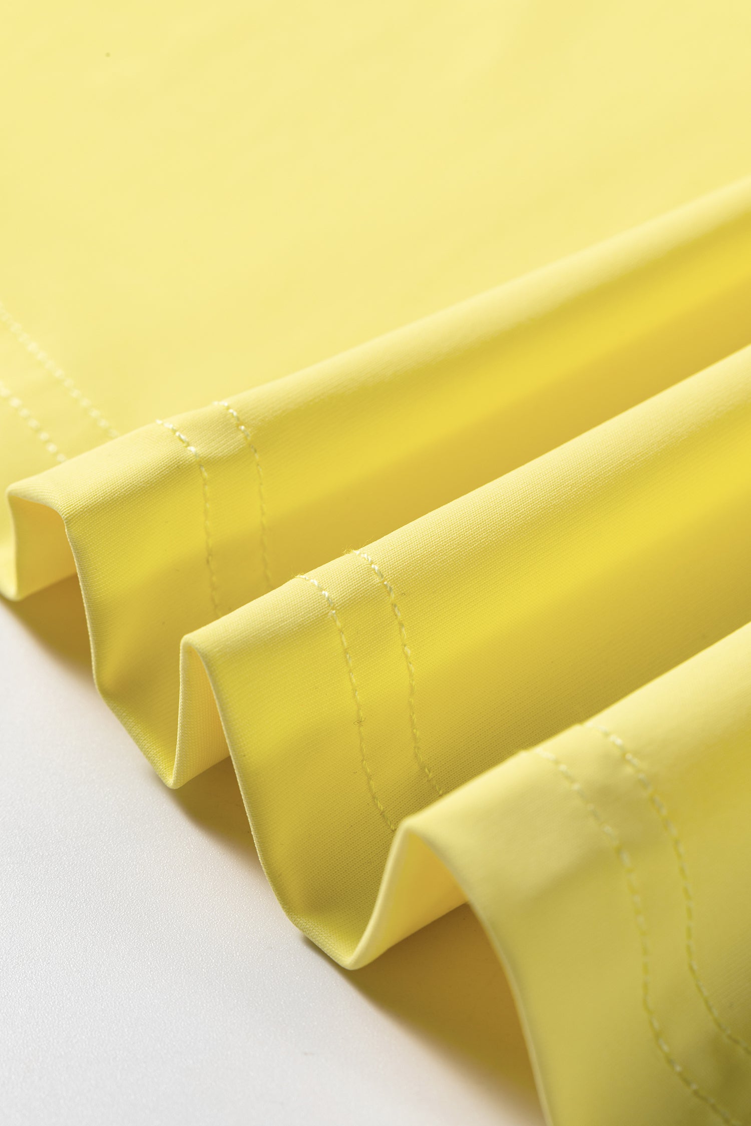 A close-up of bright yellow pleated fabric with visible stitched edges, draped diagonally against a white background.