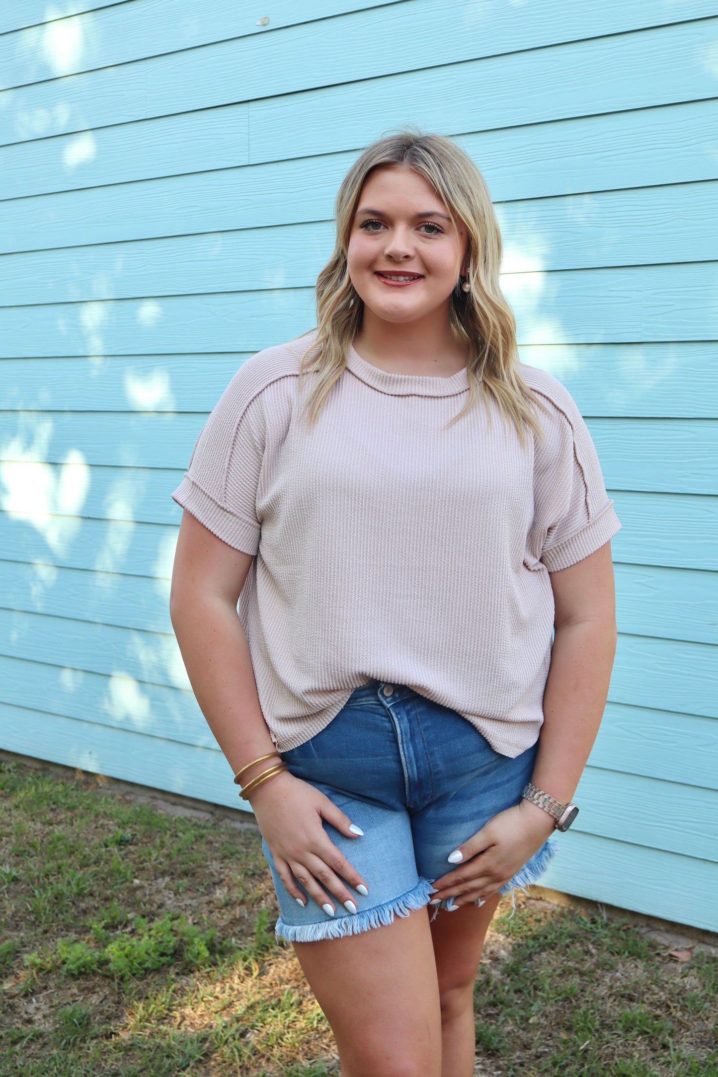 Modern Grace beige ribbed cuff sleeve top with raw edges, featuring a curved silhouette and raised texture.