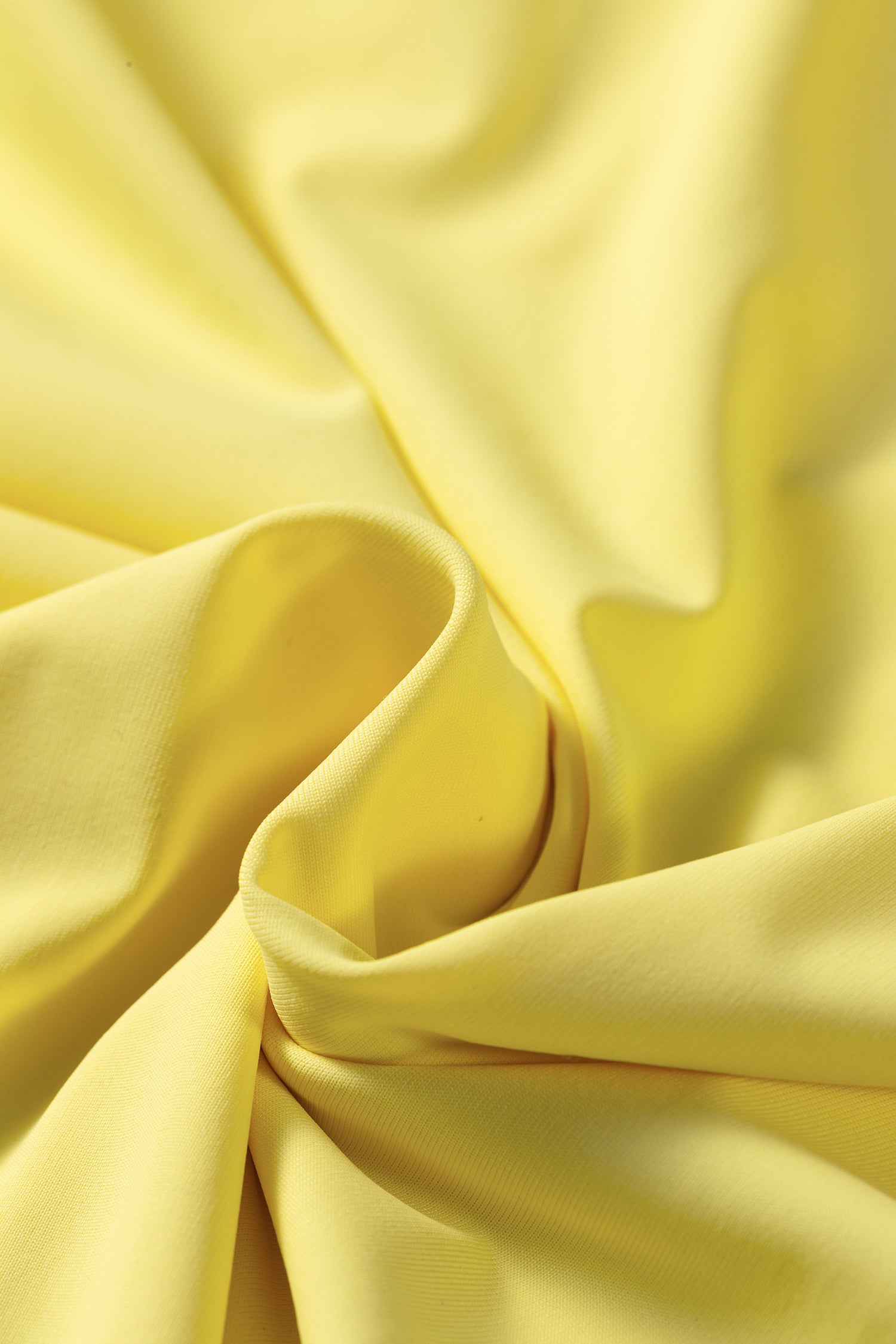 A close-up of draped yellow fabric with soft folds and a smooth satin-like sheen.