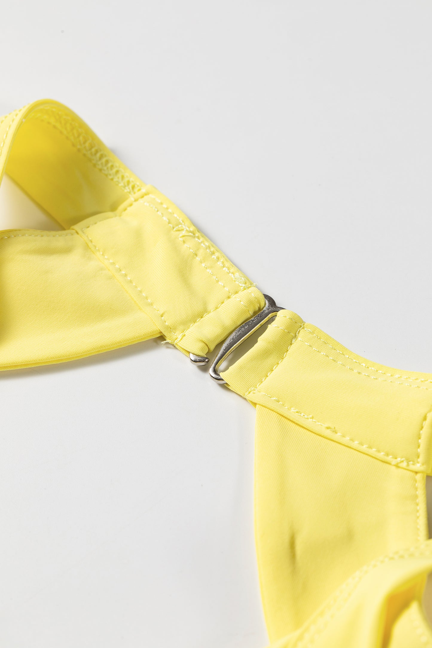 Close-up of a bright yellow bikini top strap with a silver metal grommet closure, set against a plain light gray background.