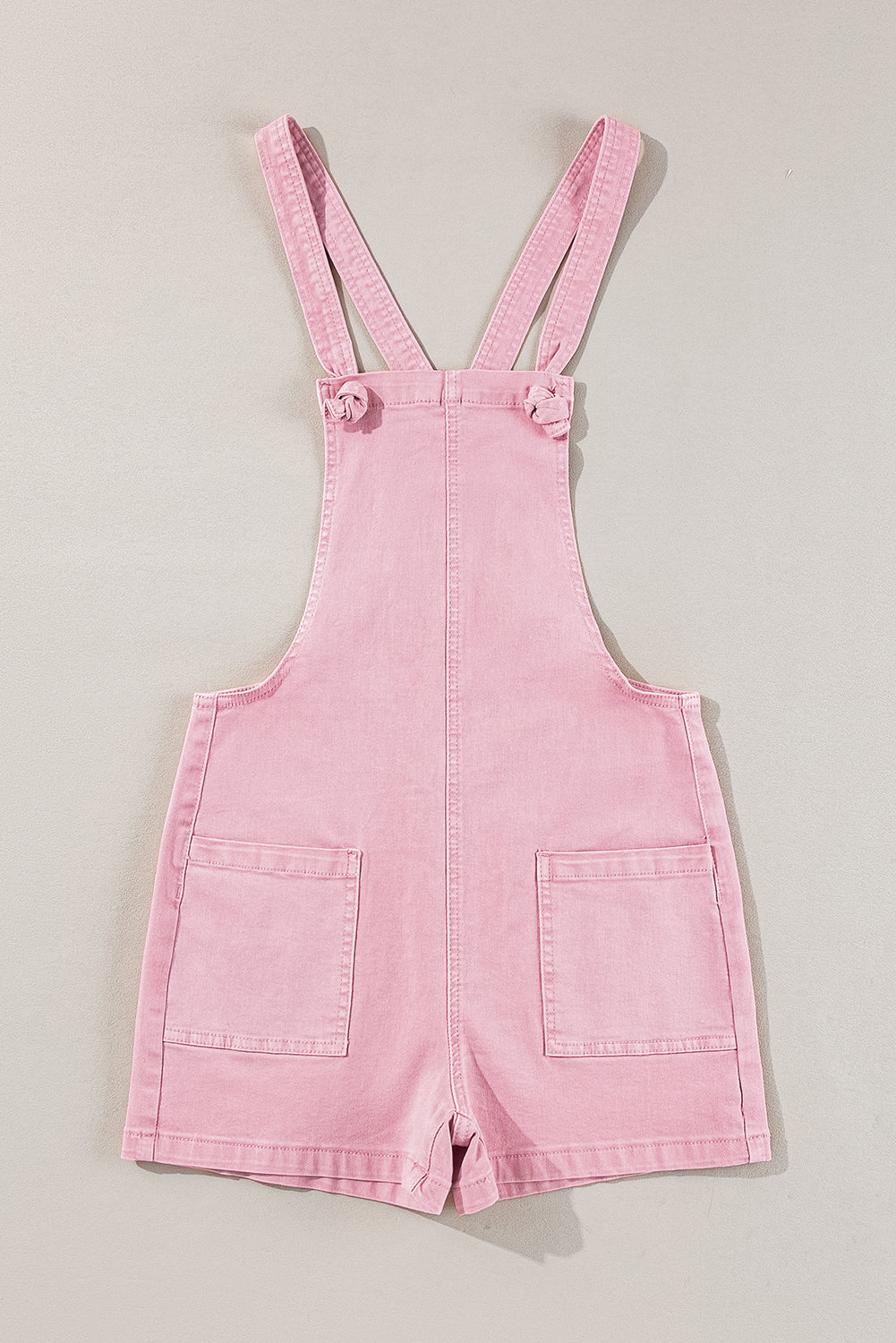 Pink solid color denim romper with knot straps, pockets, and casual fit by Modern Grace. Perfect for relaxed, stylish summer wear.