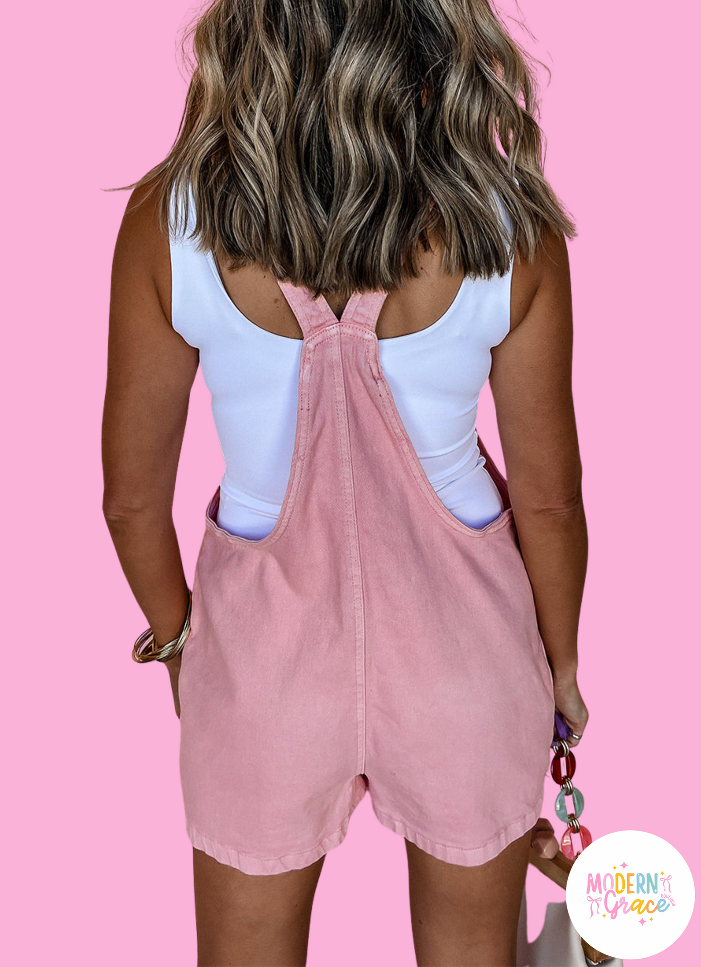 Pink solid color denim romper with knot straps, pockets, by Modern Grace, featuring cotton, polyester, viscose, and elastane fabric.