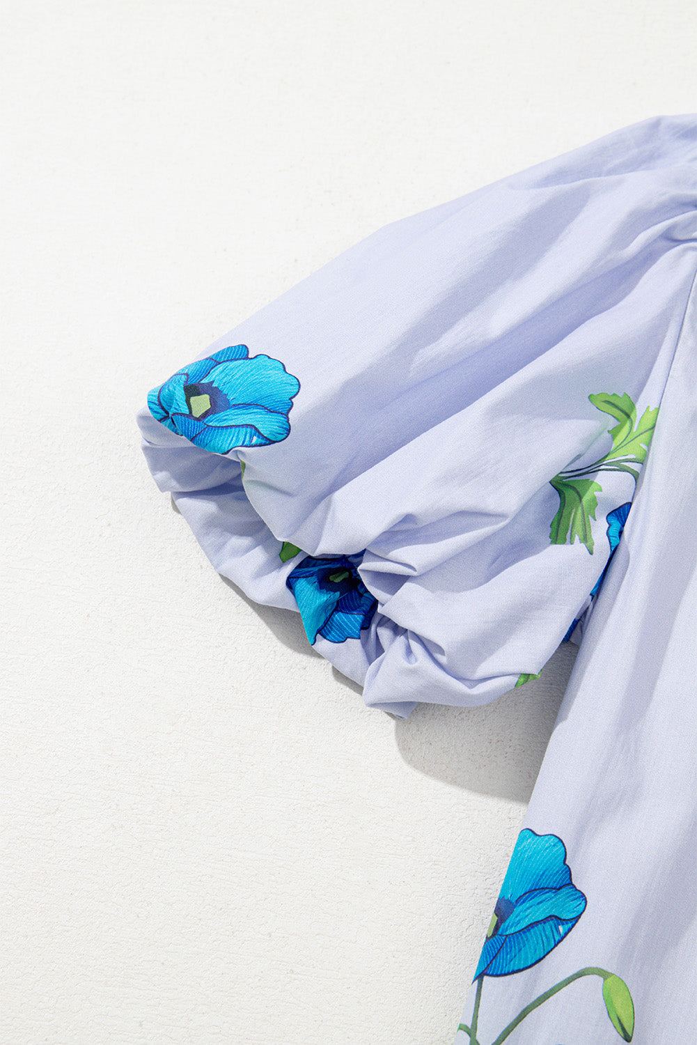 Sky blue floral print blouse by Modern Grace featuring a tie, split neck, and short puff sleeves, made of 100% cotton.