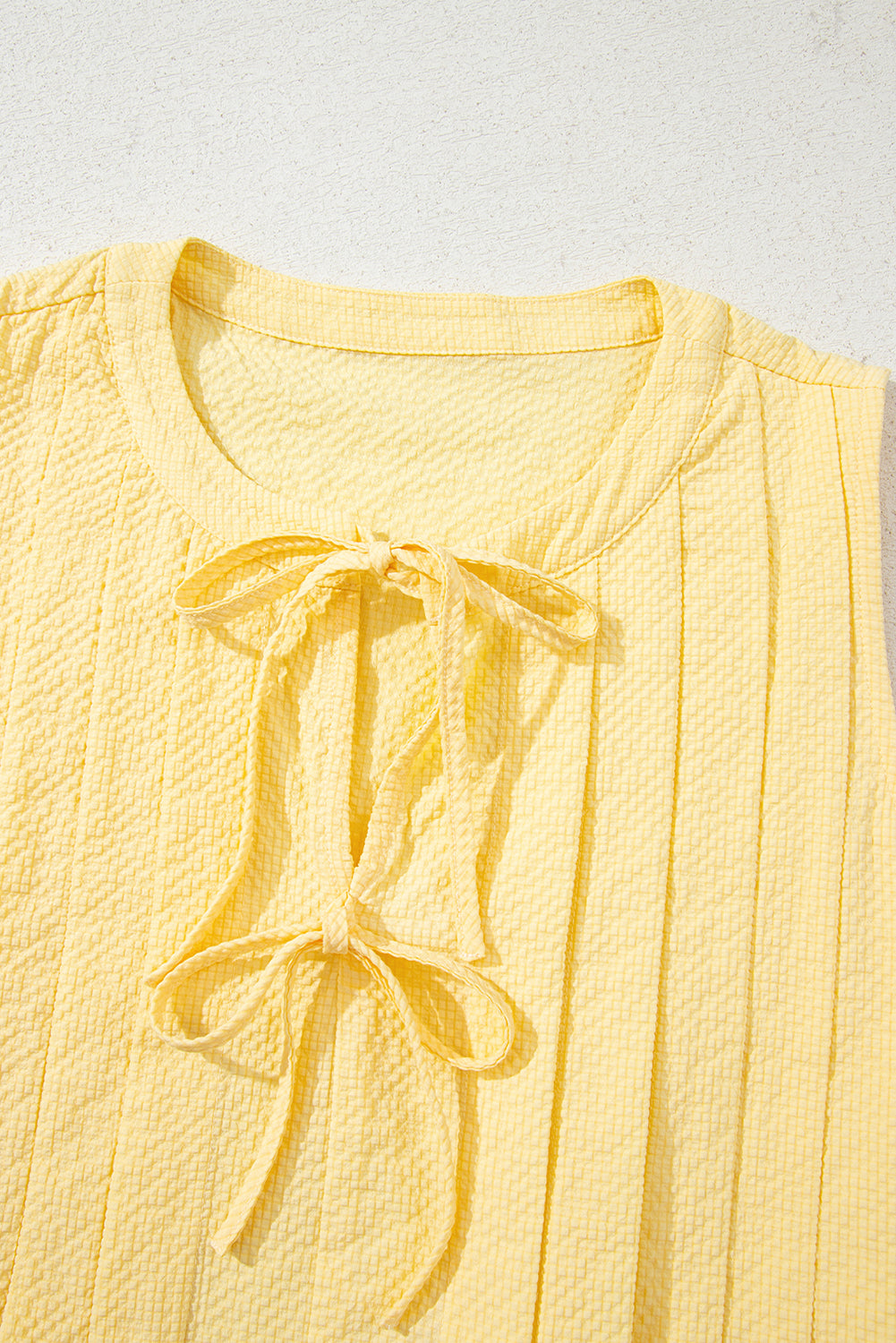 Yellow cream pleated tank top by Modern Grace featuring a bow tie and notched neck, made of 100% polyester, styled as a top.